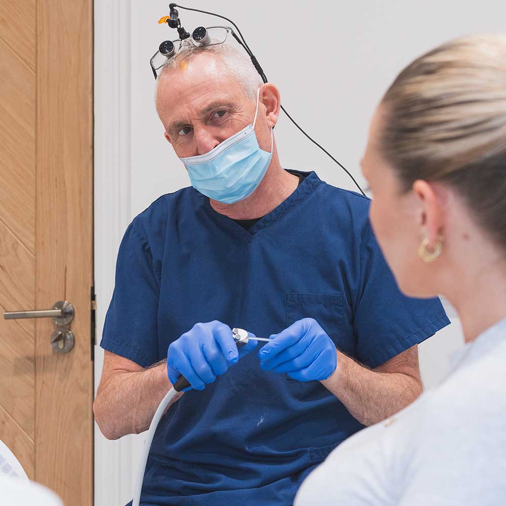 A dentist in blue scrubs and gloves with medical equipment, interacting with a woman.
