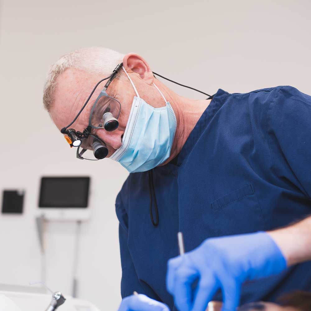 Dentist in blue scrubs and face mask using dental tools in a clinical setting