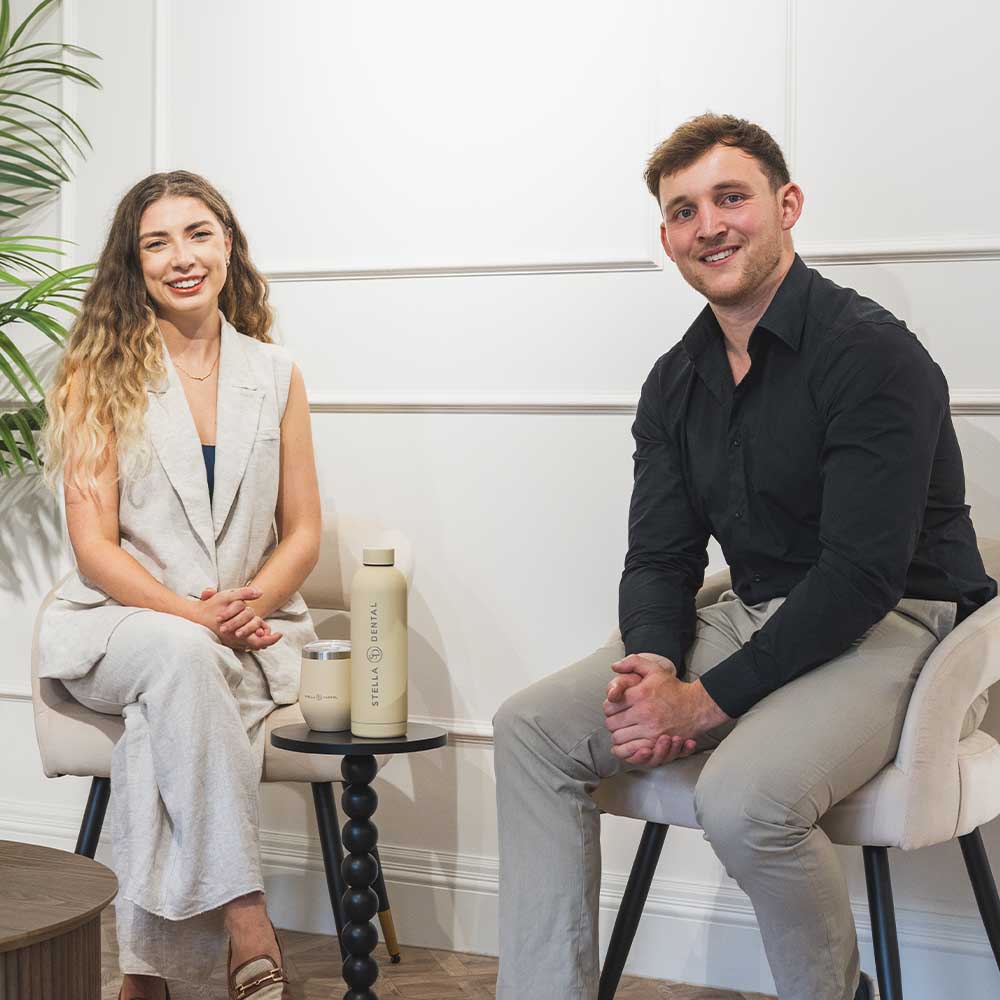 Two people sitting in chairs with a small table between them, featuring a bottle on the table.