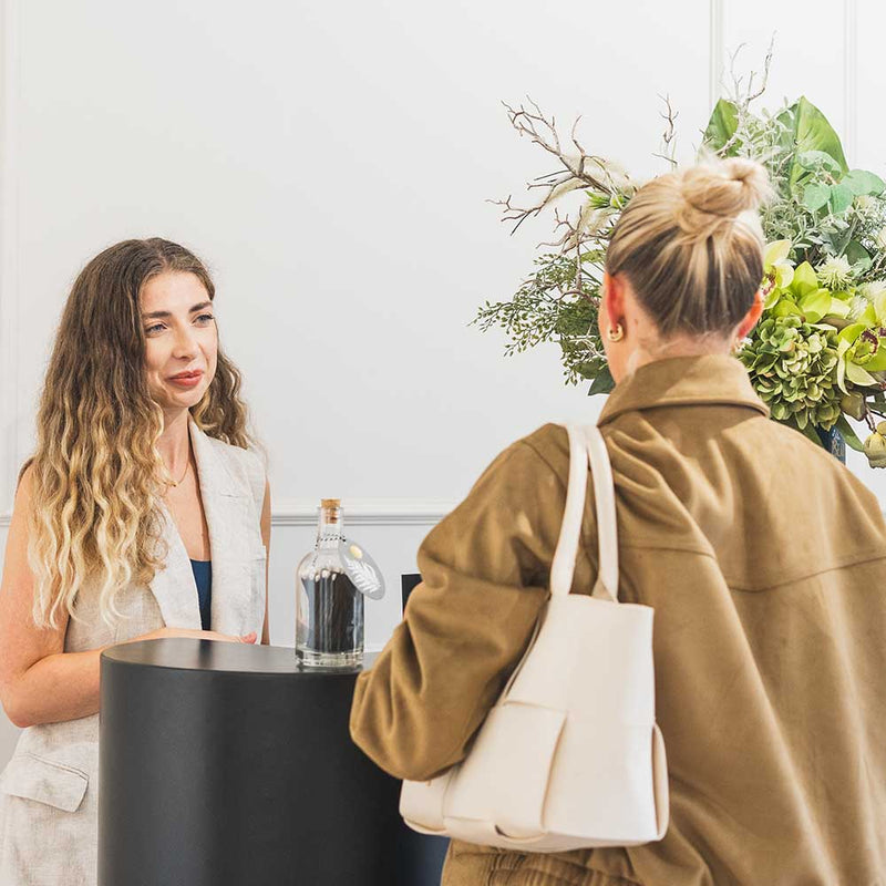 Two women interacting at a reception with a decorative plant in the background