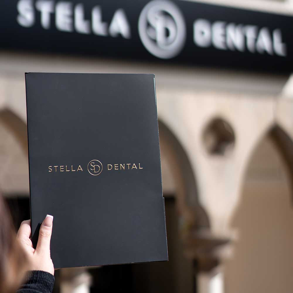 Person holding a black folder with 'Stella Dental' logo in front of a dental office entrance.
