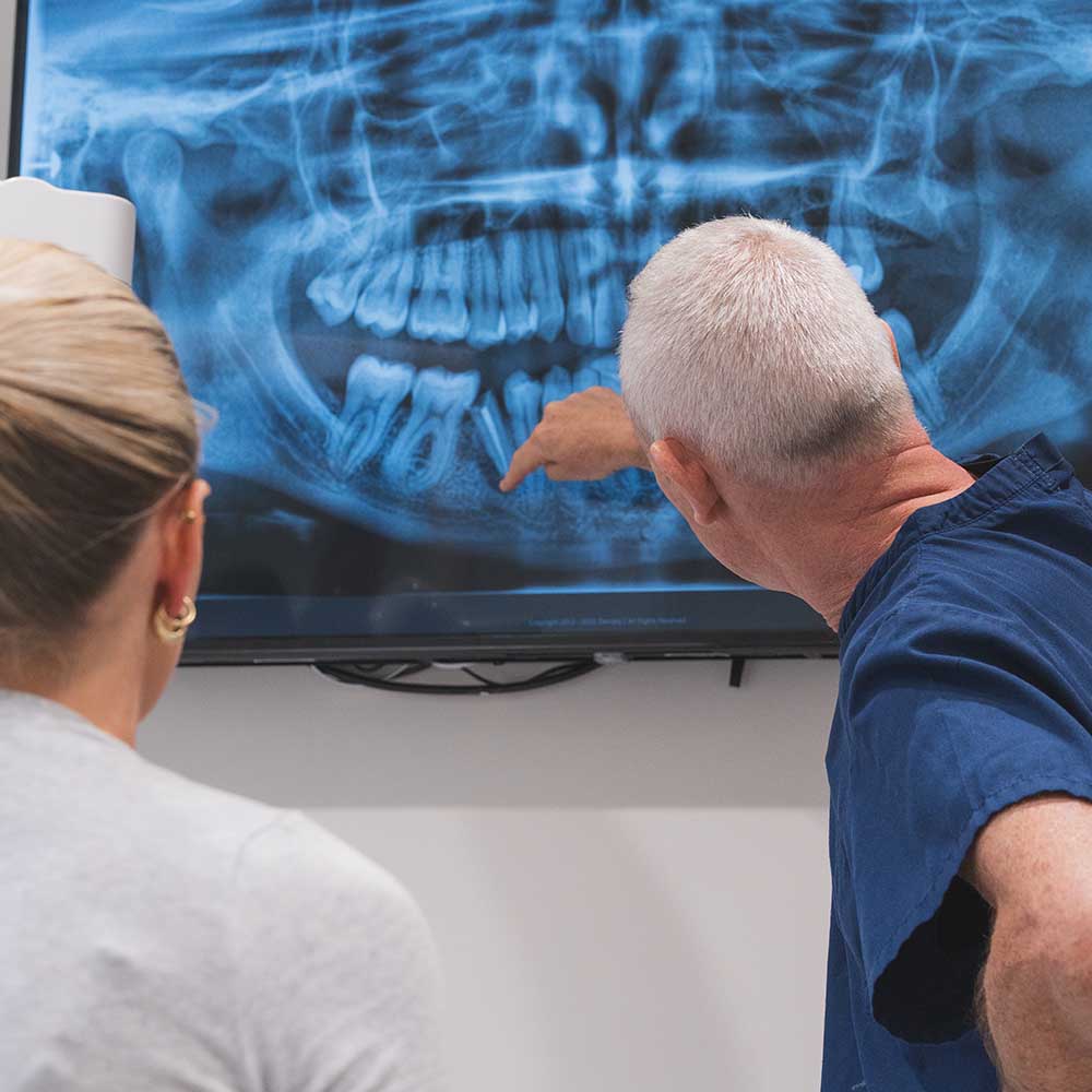 Two people examining an x-ray of teeth on a screen.