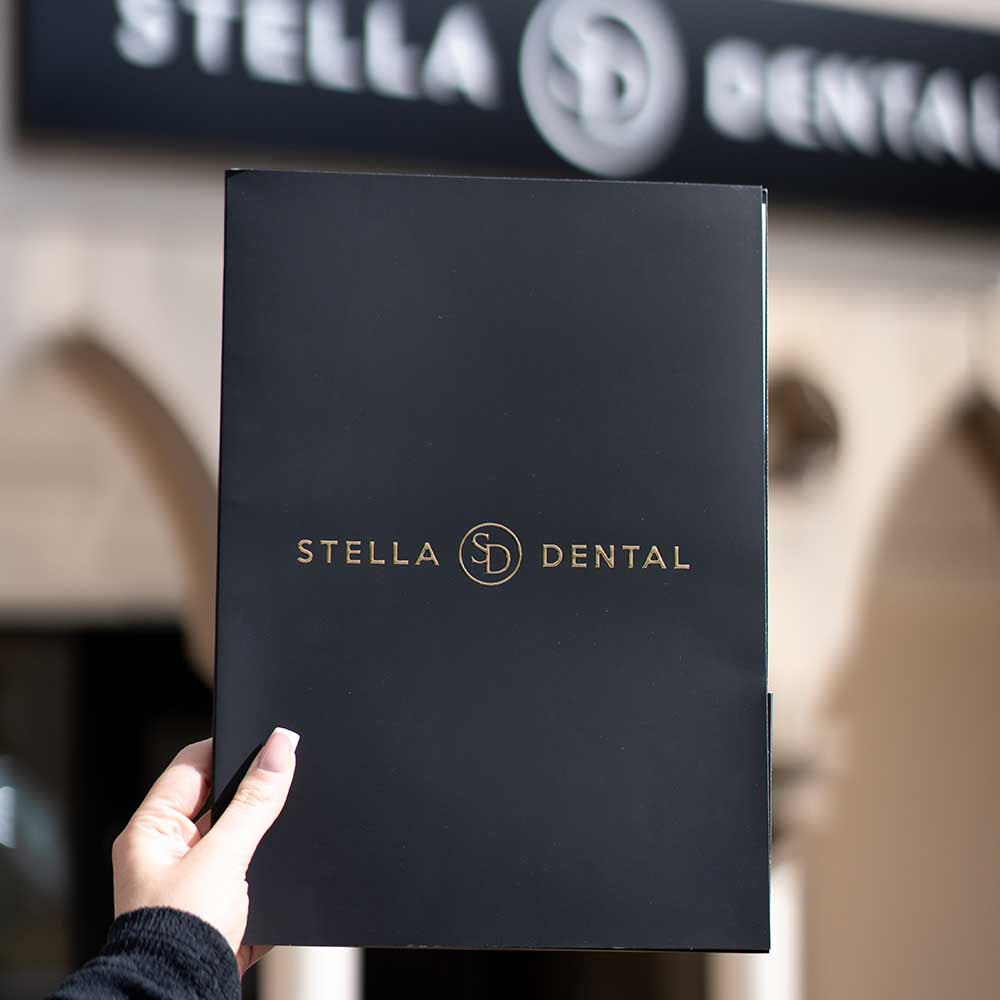 Black folder with 'Stella Dental' logo held in front of a dental office entrance.