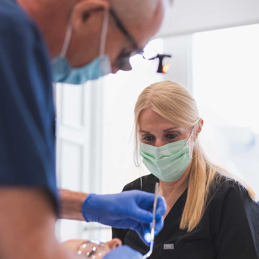 Dental professional examining a patient with dental tools, wearing protective gear.