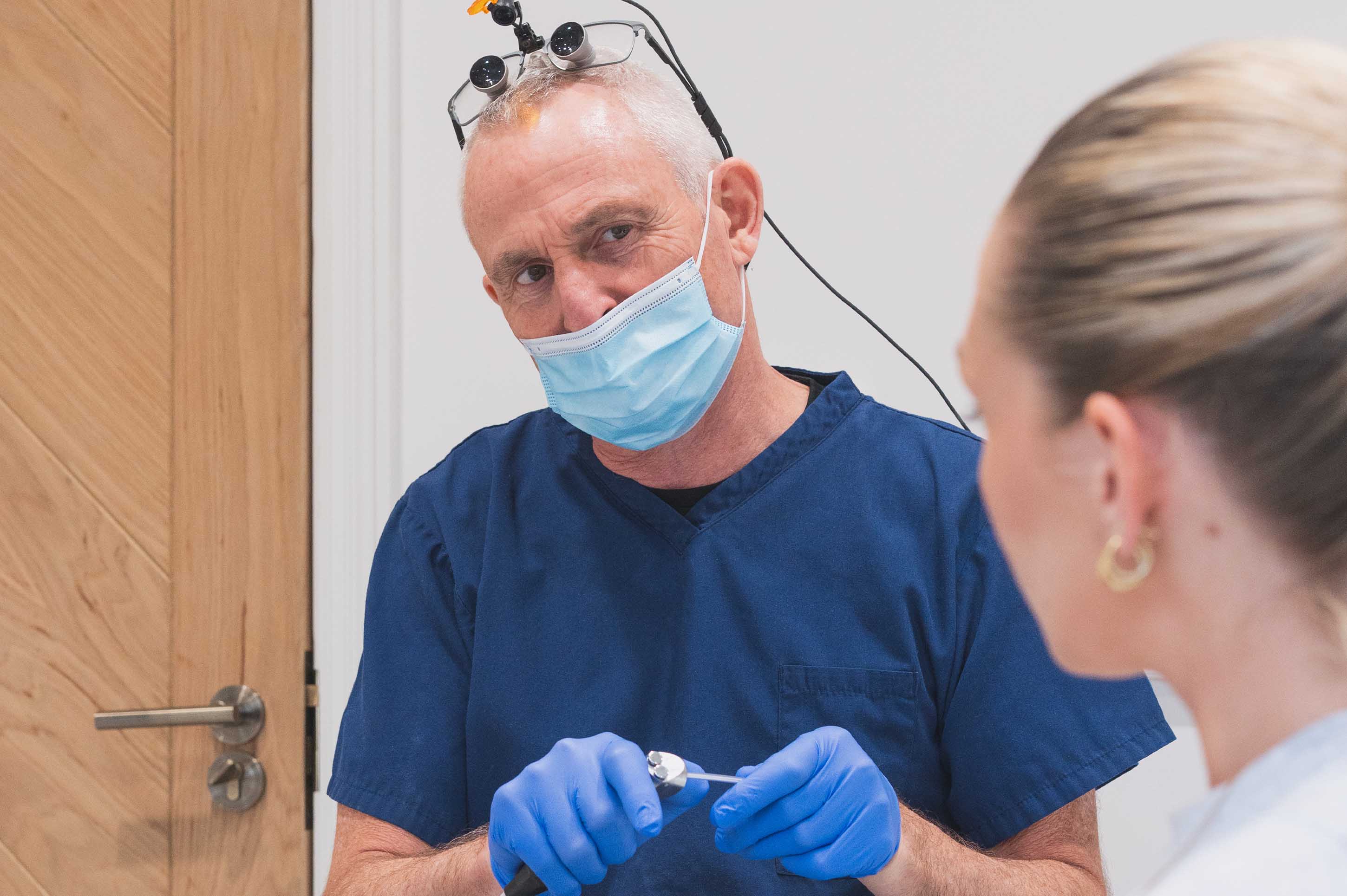 A dentist in blue scrubs and gloves wearing a face mask
